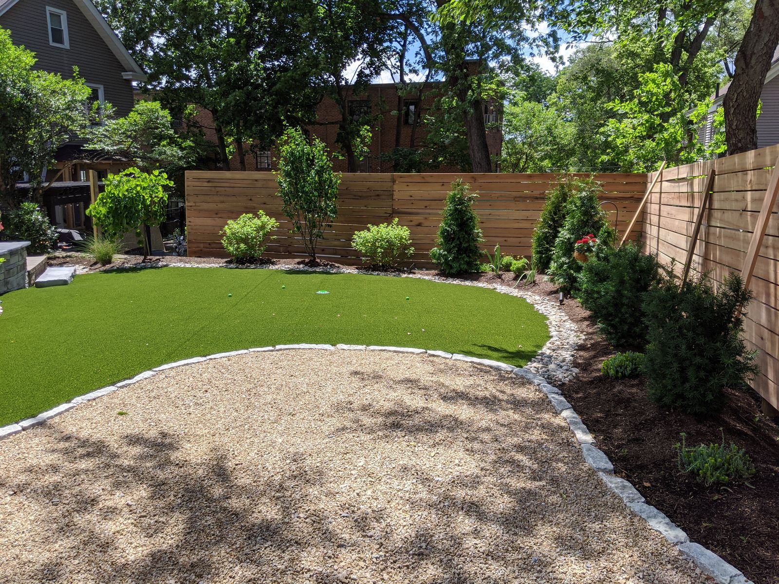 Curved artificial turf lawn bordered by gravel path and cedar fence