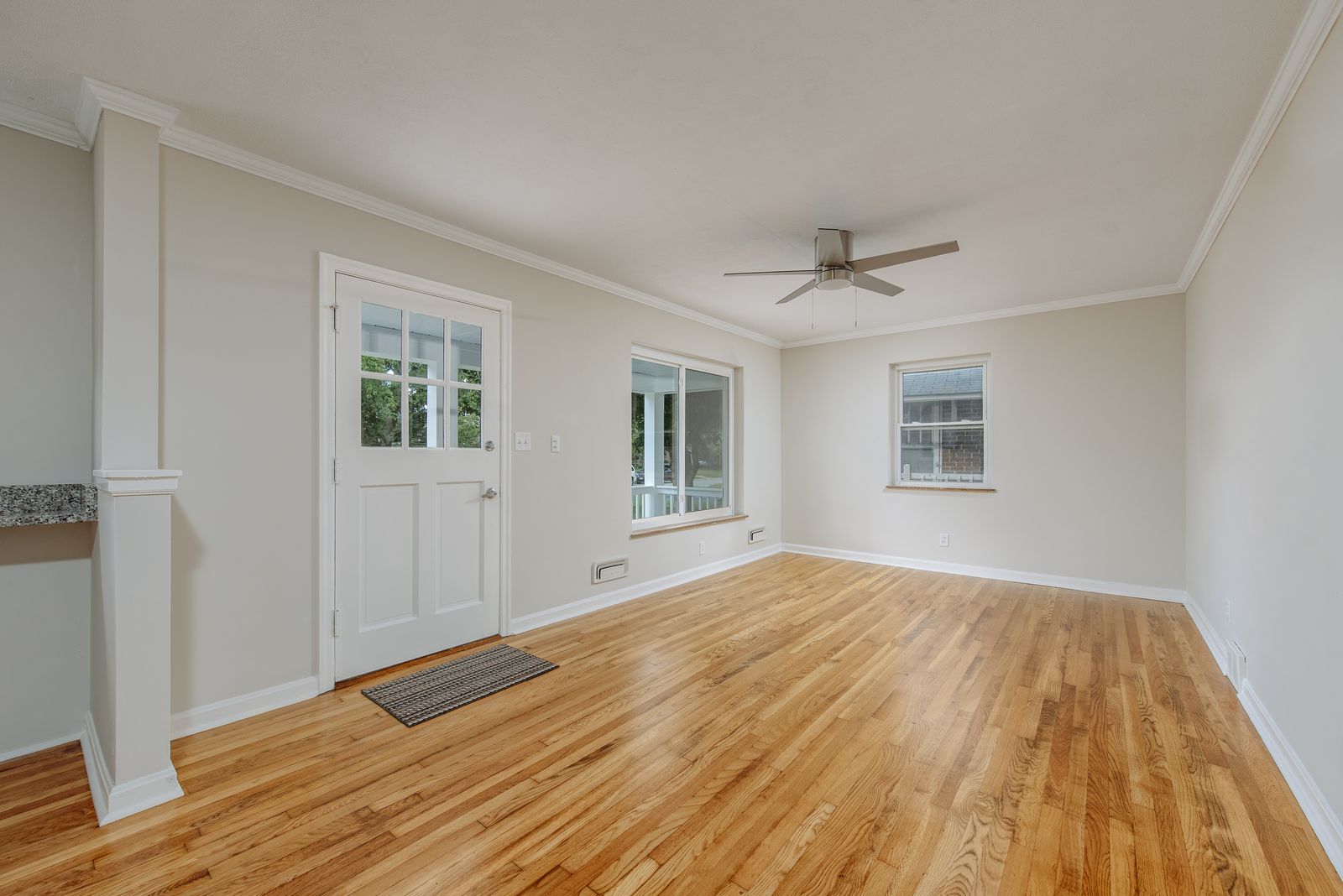 Bright living room with refinished hardwood floors, white entry door, ceiling fan, and crown molding