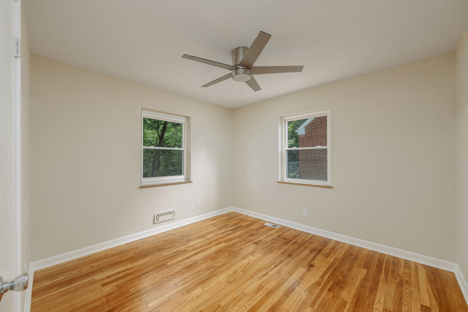 Main-floor bedroom with refinished hardwood floors, two windows, and a modern ceiling fan