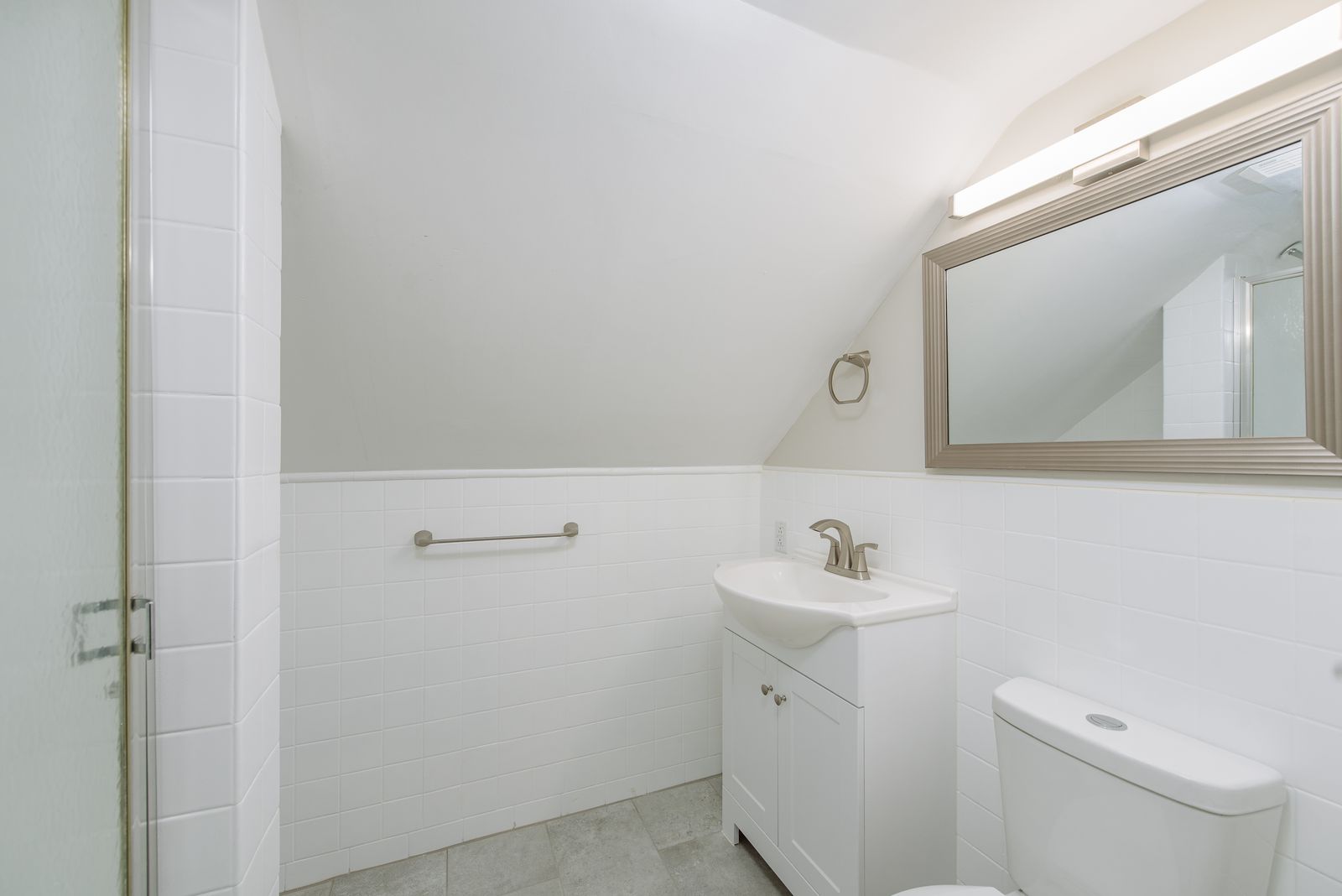 Upstairs half bath with a white vanity, framed mirror, subway tile wainscot, and a walk-in shower