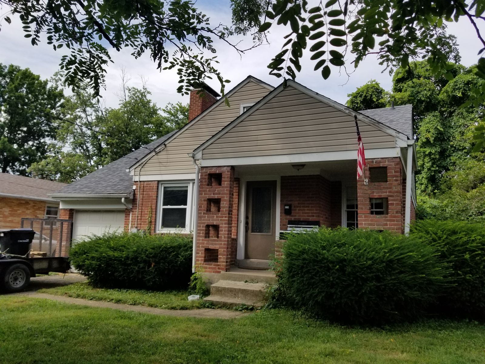 Cottage front exterior before renovation with aging brick and overgrown hedges