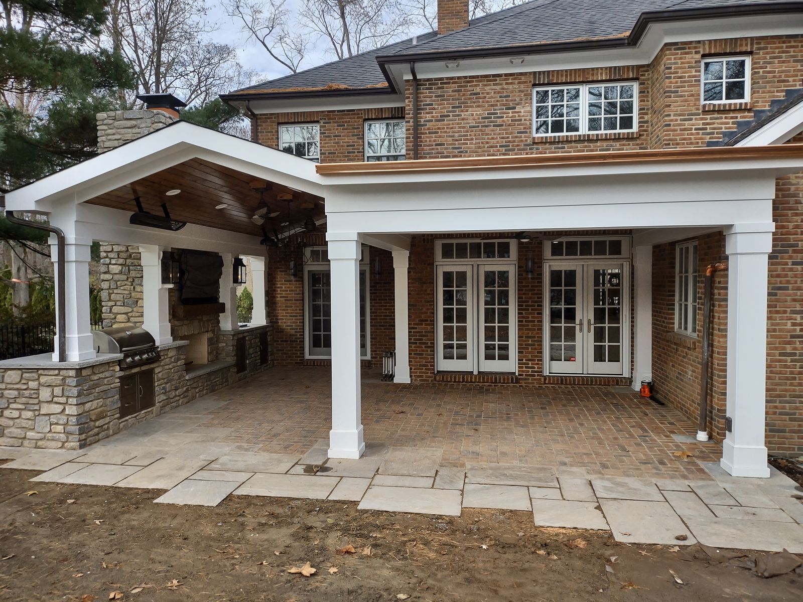 Gable-roofed covered porch with white columns, stone bases, and brick paver floor attached to a brick home