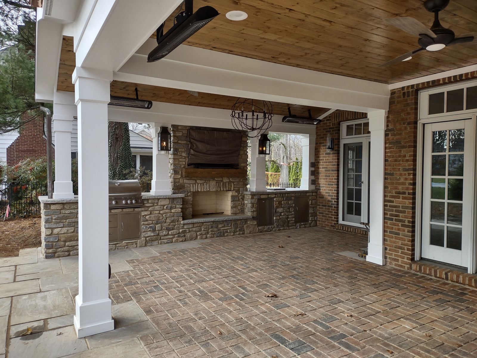 Covered porch interior with outdoor kitchen, stone fireplace, ceiling fan, and wood ceiling