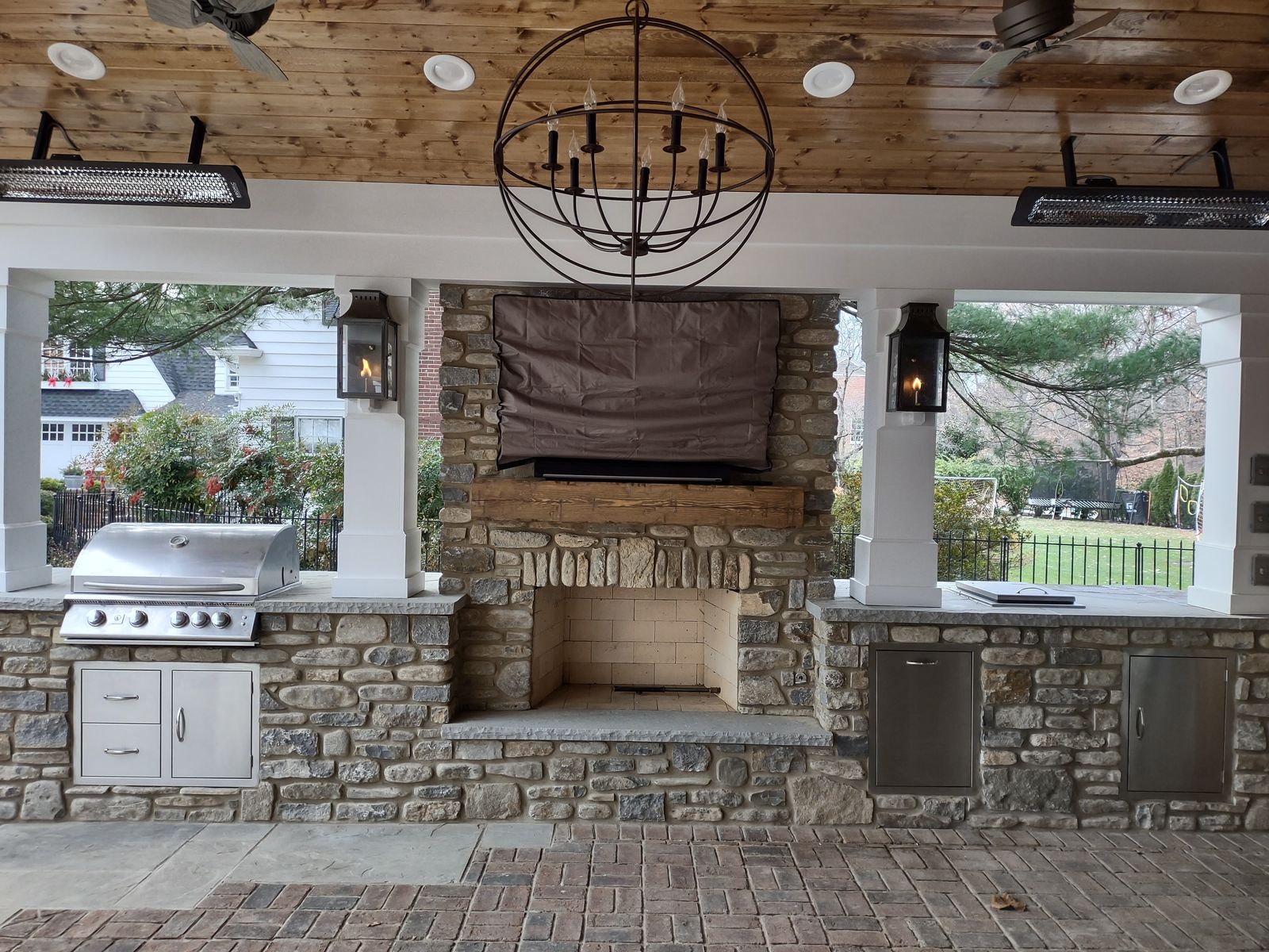 Built-in grill and stone fireplace with wall-mounted TV under a covered porch