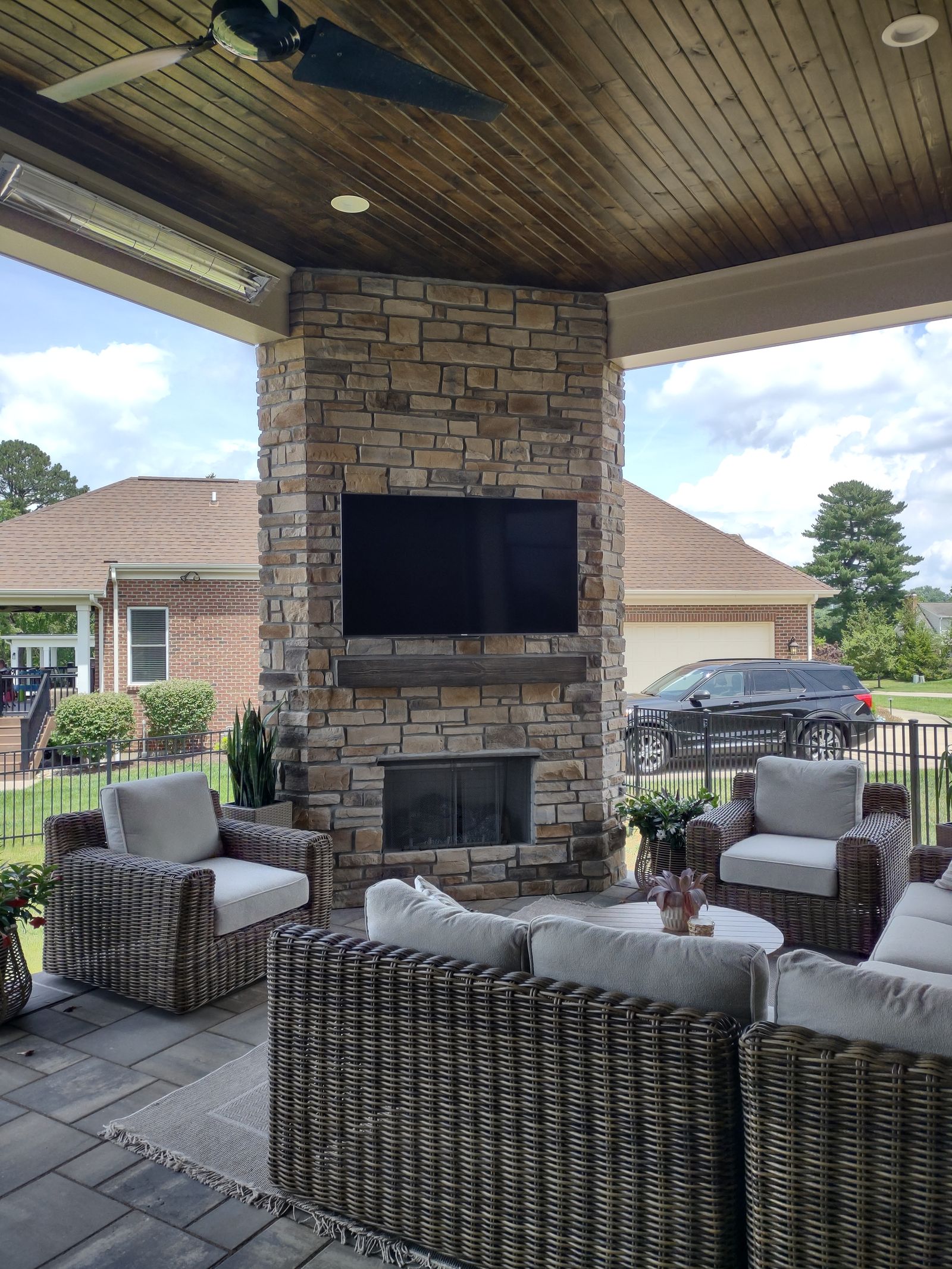 Covered porch lounge with stone fireplace, TV, and wicker seating