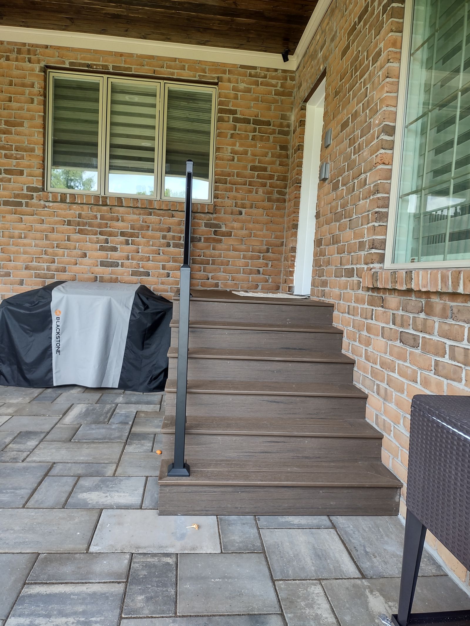 Composite deck steps leading from a paver patio up to the covered porch