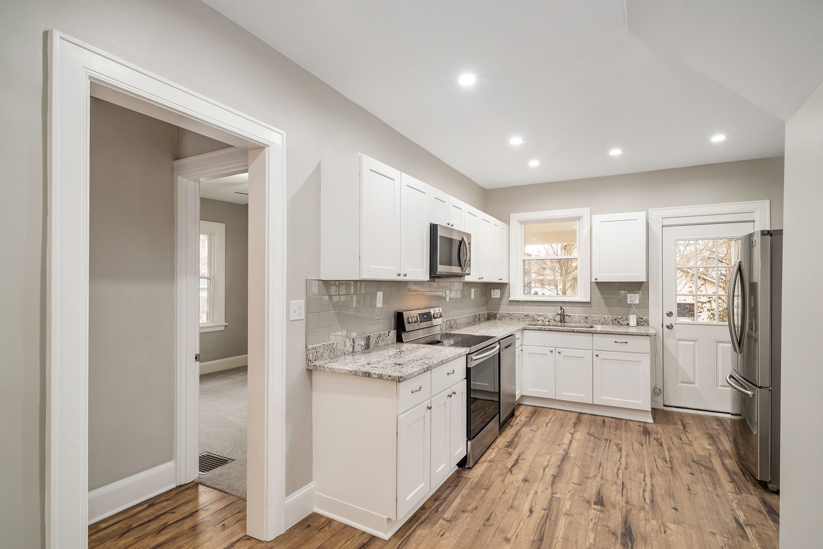 New kitchen with white shaker cabinets, granite-look countertops, gray subway tile backsplash, and stainless steel appliances