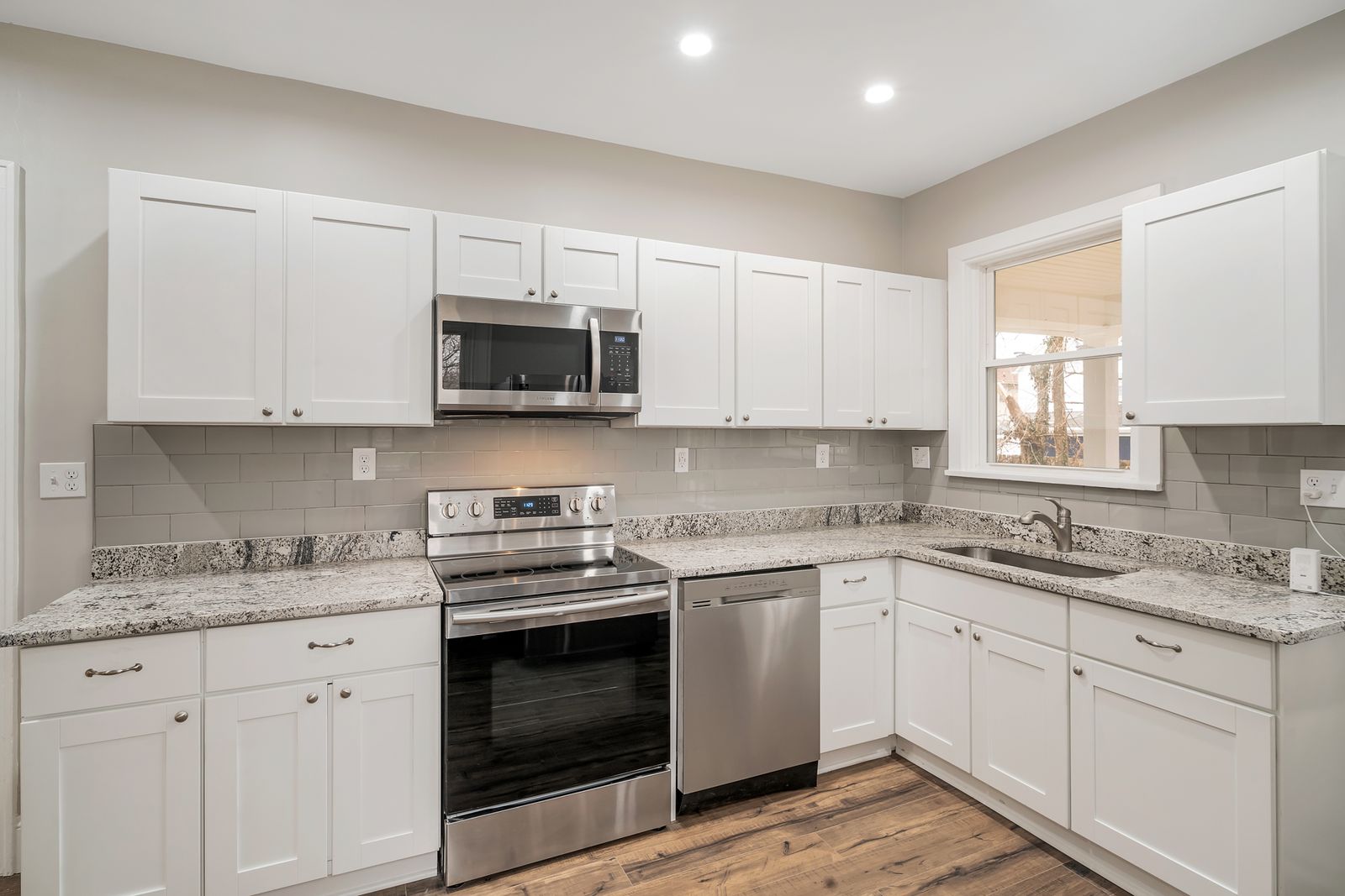 Straight-on view of the new kitchen's white shaker cabinetry, stainless range and dishwasher, and undermount sink