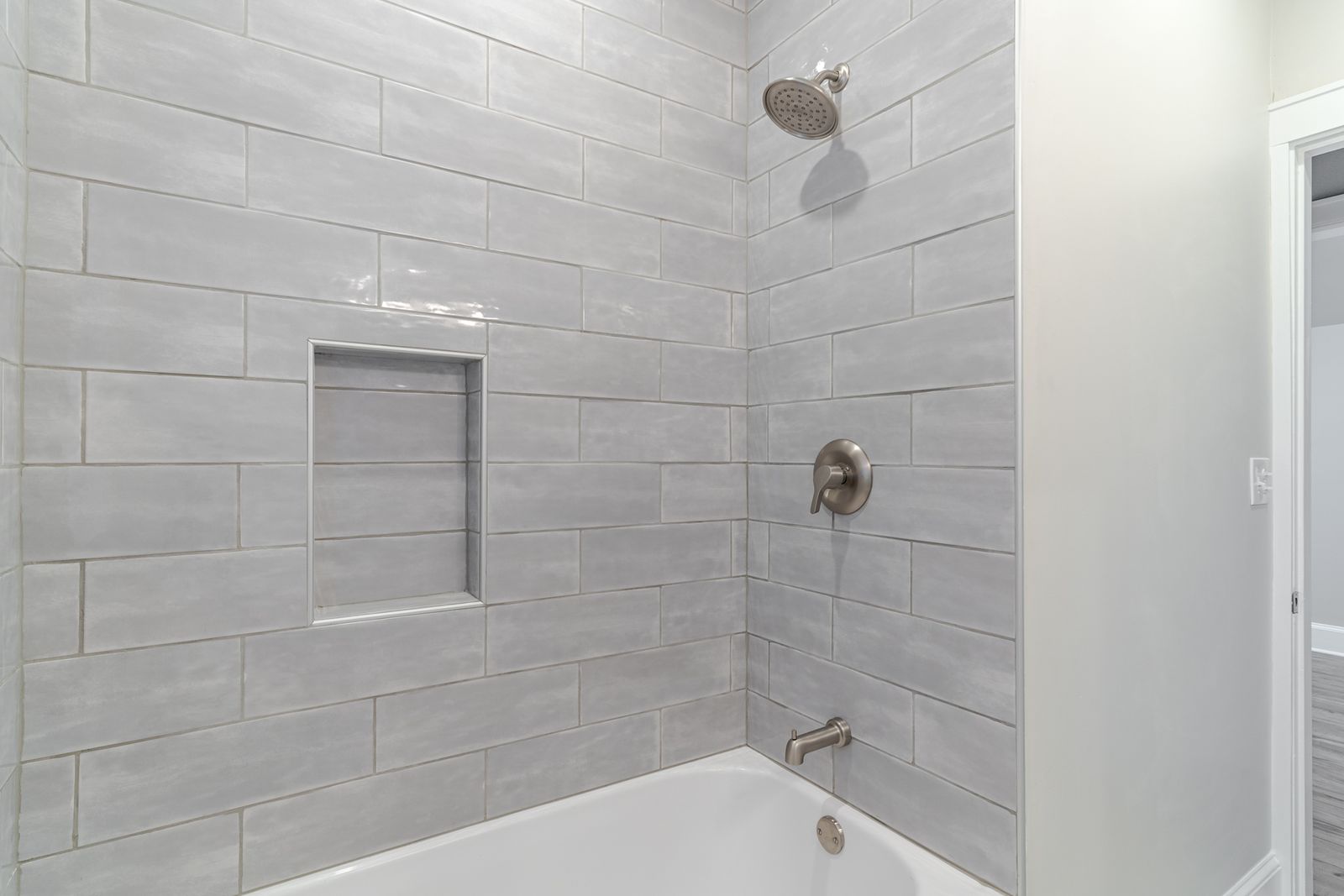 New tub and shower surround in large-format light gray tile with a recessed niche and brushed nickel fixtures