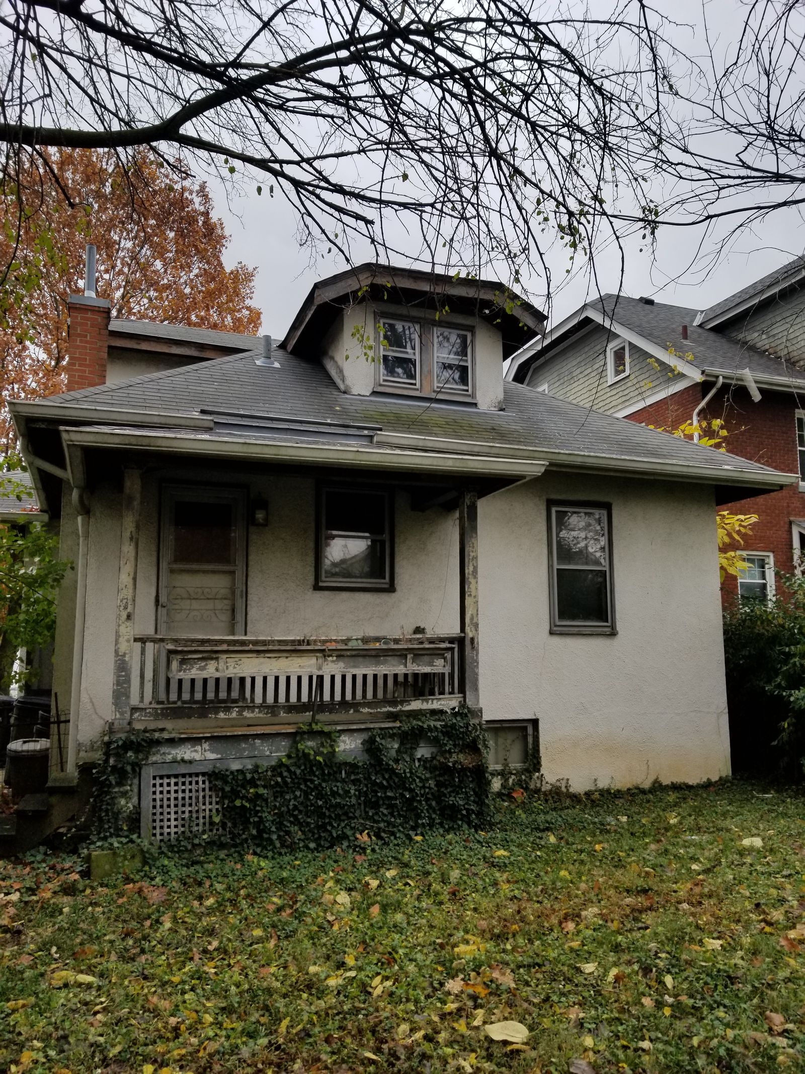 Rear of the bungalow before renovation, with stained stucco, a rotting porch railing, and overgrown ivy