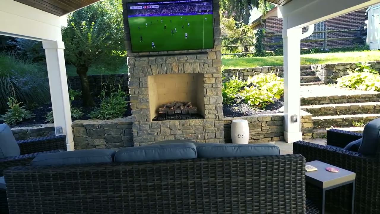 A covered patio with stone fireplace and lounge seating, set to music.