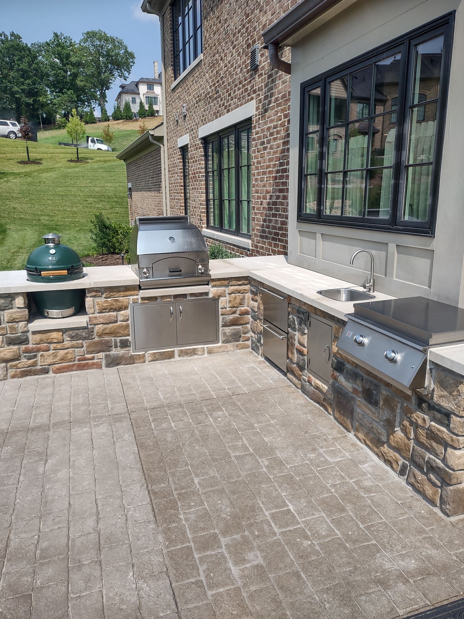 Stone-clad outdoor kitchen with built-in grill on a paver patio