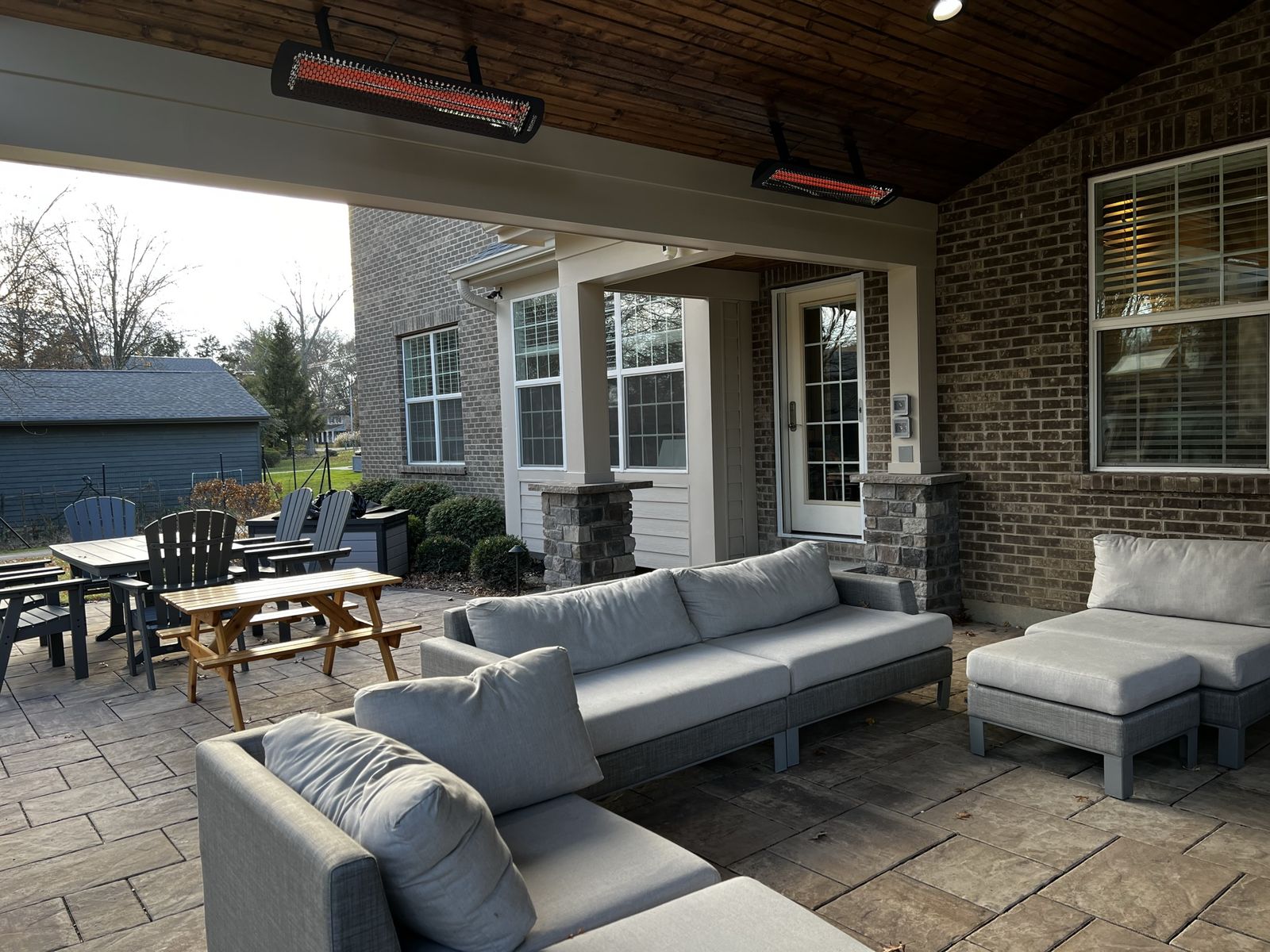 Covered outdoor living room with sofas, heaters, and dining set