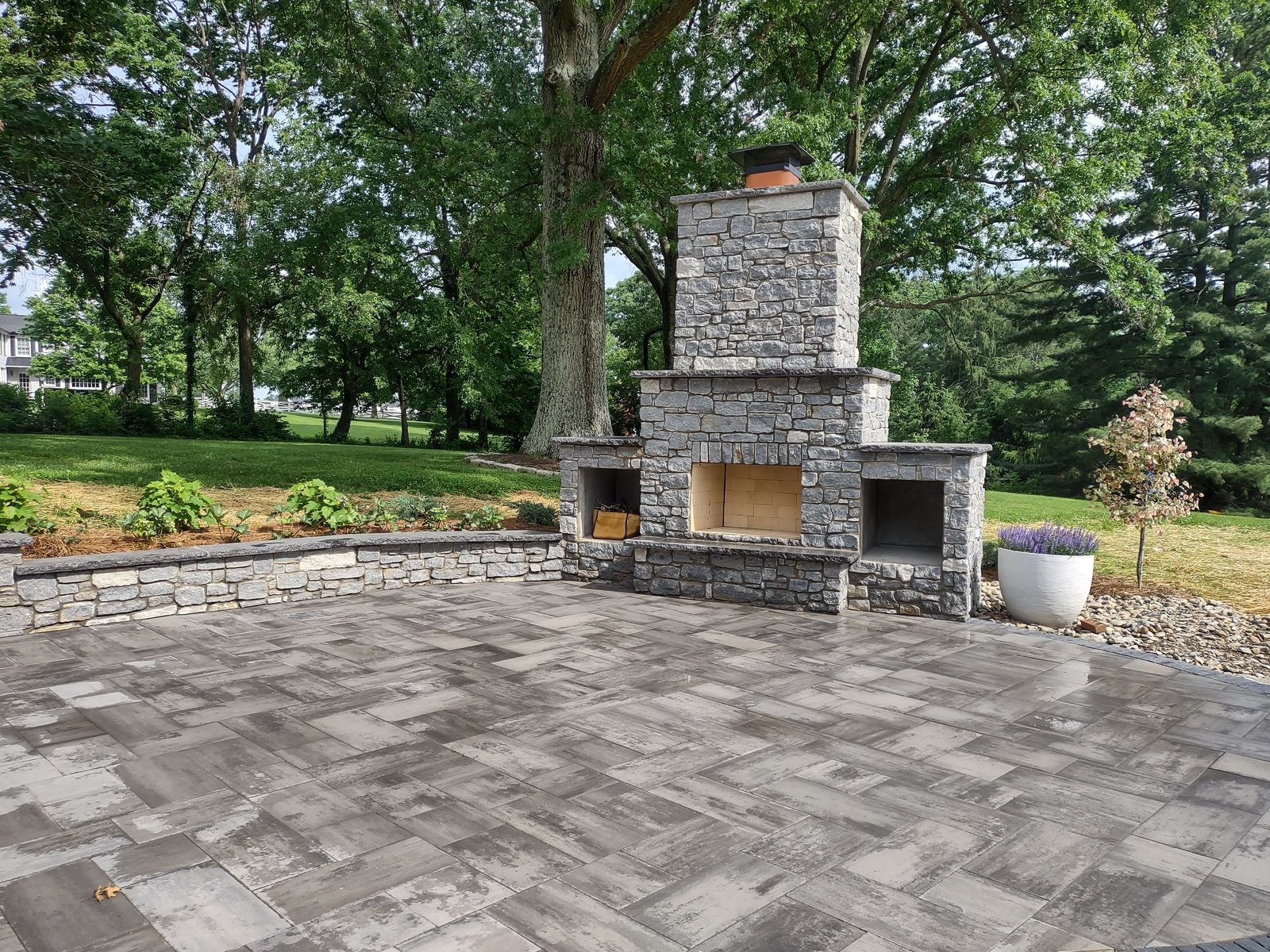 Stone outdoor fireplace with wood storage boxes on a paver patio