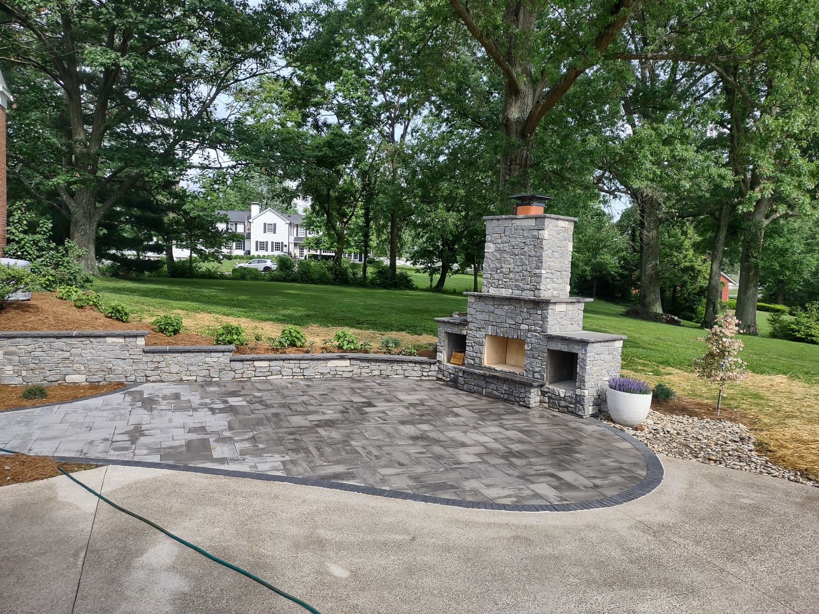 Curved paver patio with outdoor stone fireplace and manicured lawn