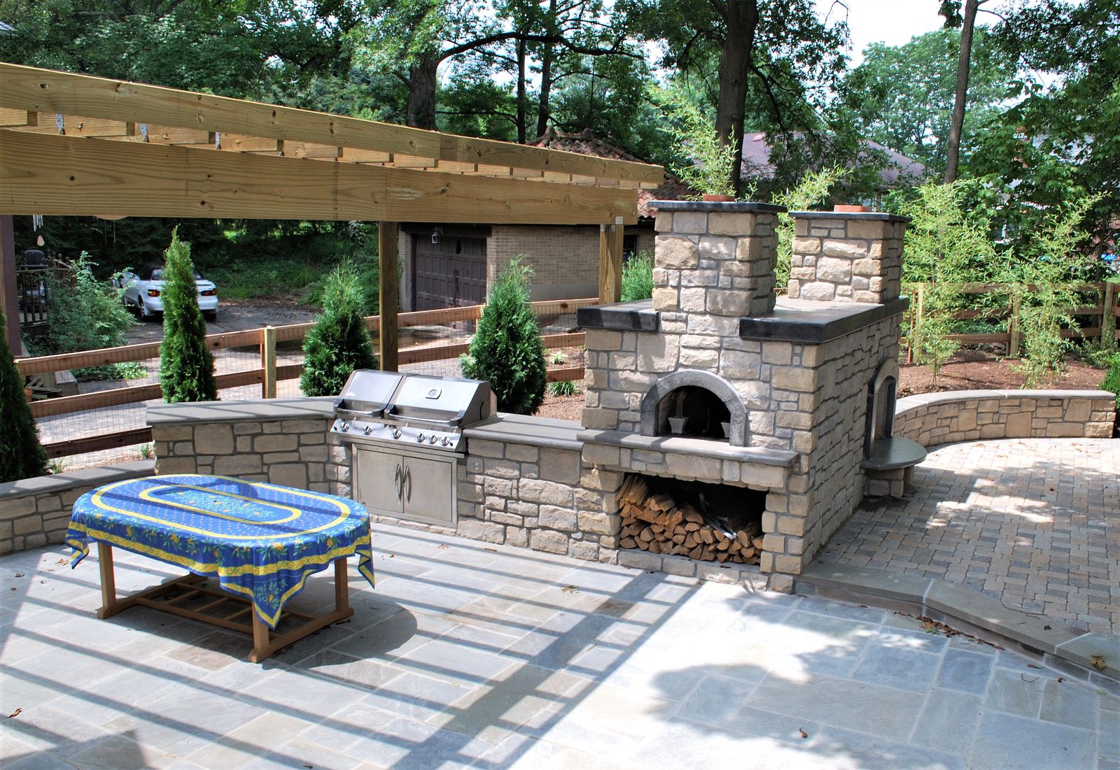 Timber pergola over a stone grill island and outdoor fireplace