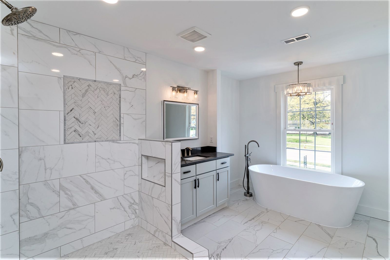 Master bath with freestanding tub, marble-look tile, glass shower, and dark vanity
