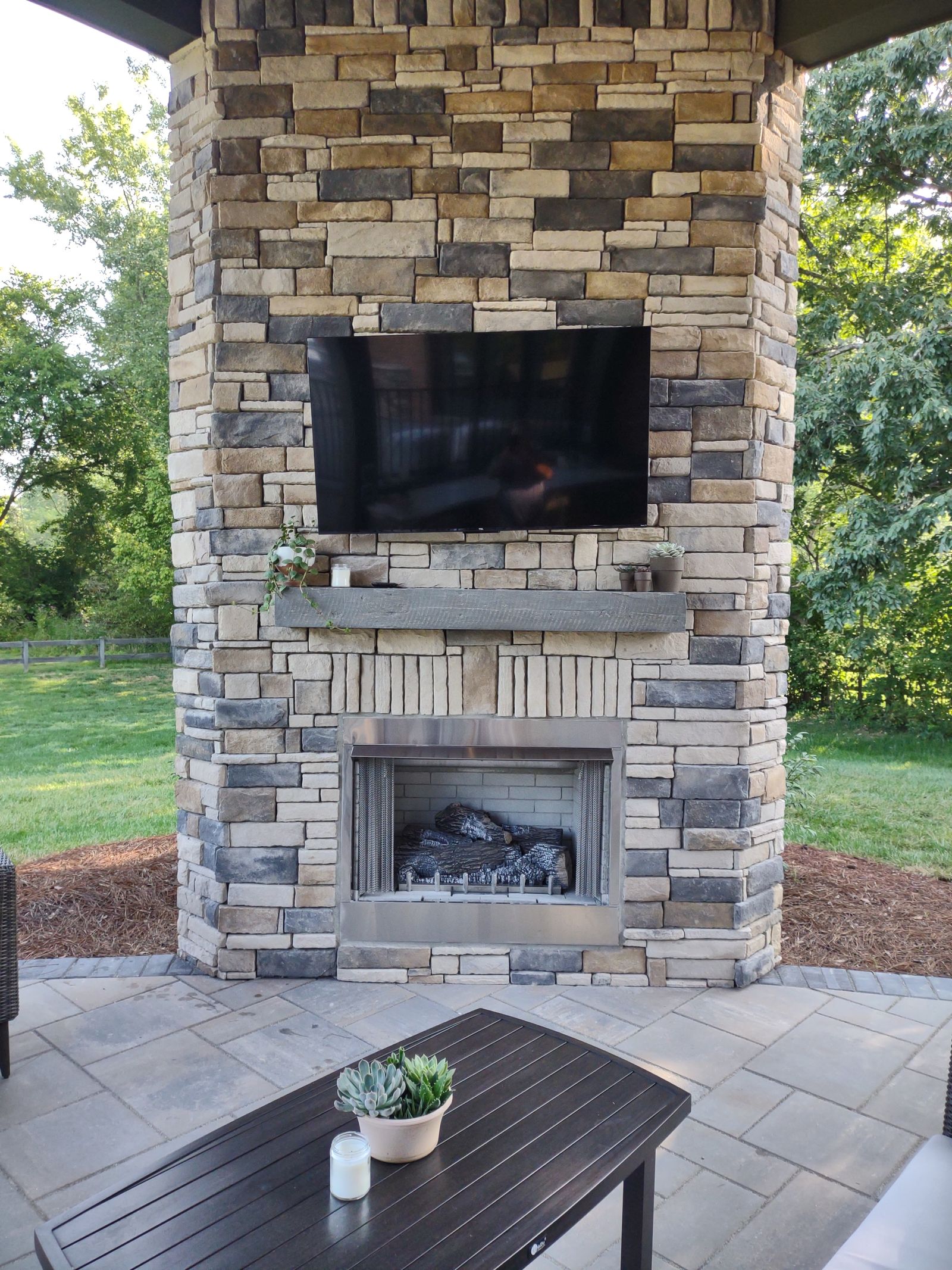 Stone fireplace with wall-mounted TV beside an outdoor dining table
